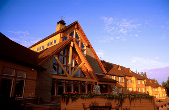 Exterior view of the entrance to a large stone and wooden lodge at sunset