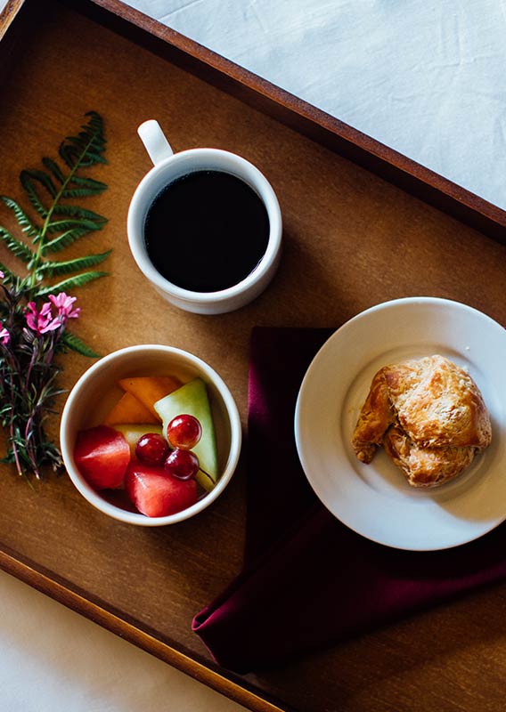 A food tray with small breakfast items on a white bedspread.