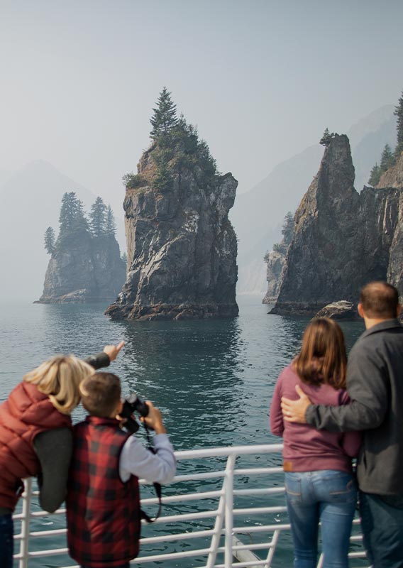 A group of people look out from a boat deck at a rocky coastline.