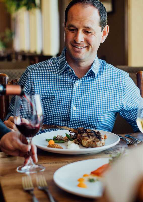 A server pours wine for a guest at a dinner table.
