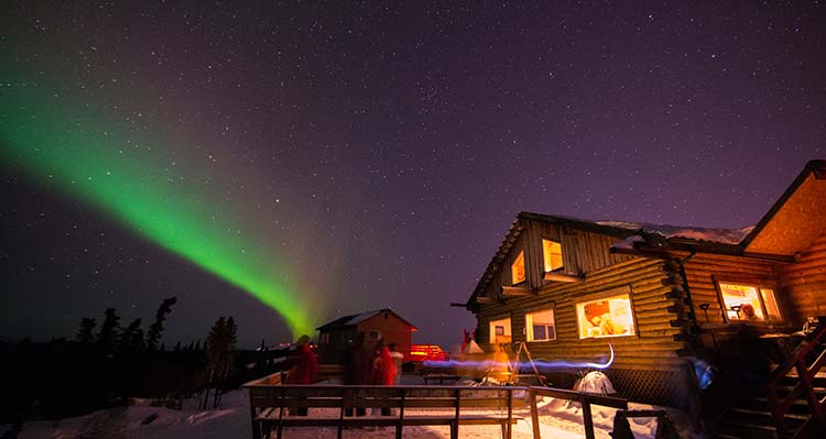 A green aurora pipe in the night sky being viewed by guests at Talkeetna Alaskan Lodge.