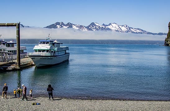 People on a shore while a Kenai Fjords Boat is docked closeby.