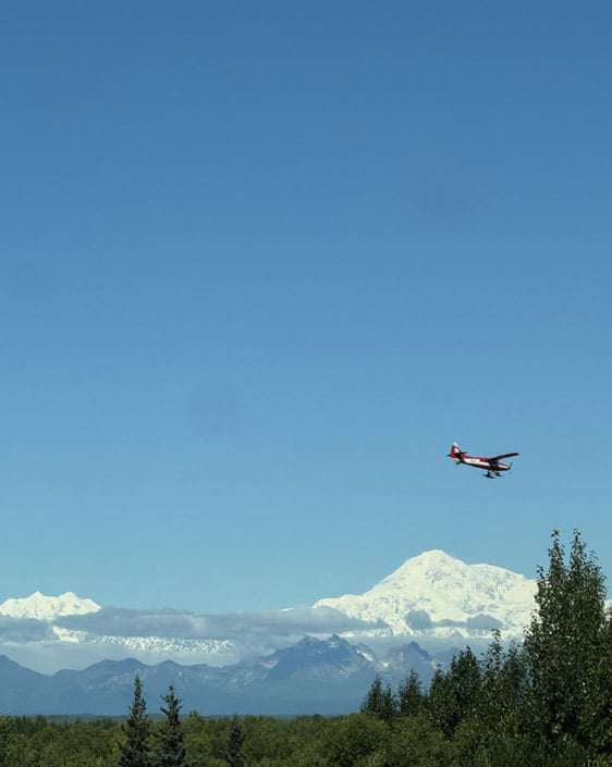 A propeller plane flying over Talkeetna with Denali Mountain in the background