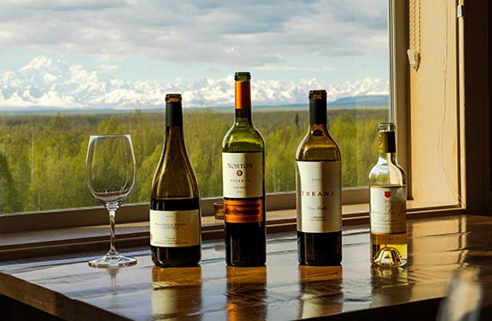 Four wine bottles on a table by a window.
